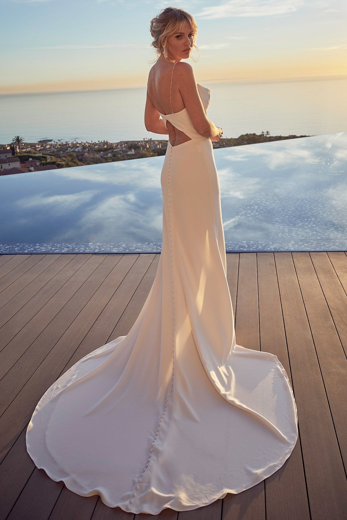 A woman in a wedding dress is standing next to a pool overlooking the ocean.
