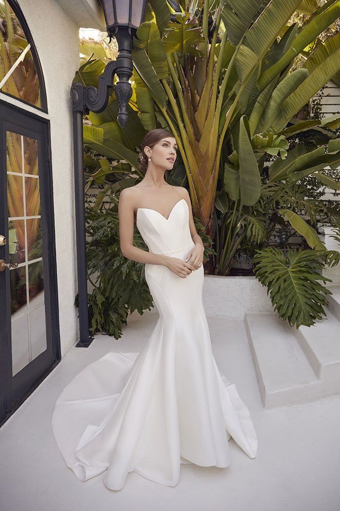 A woman in a white wedding dress is standing in front of a building.