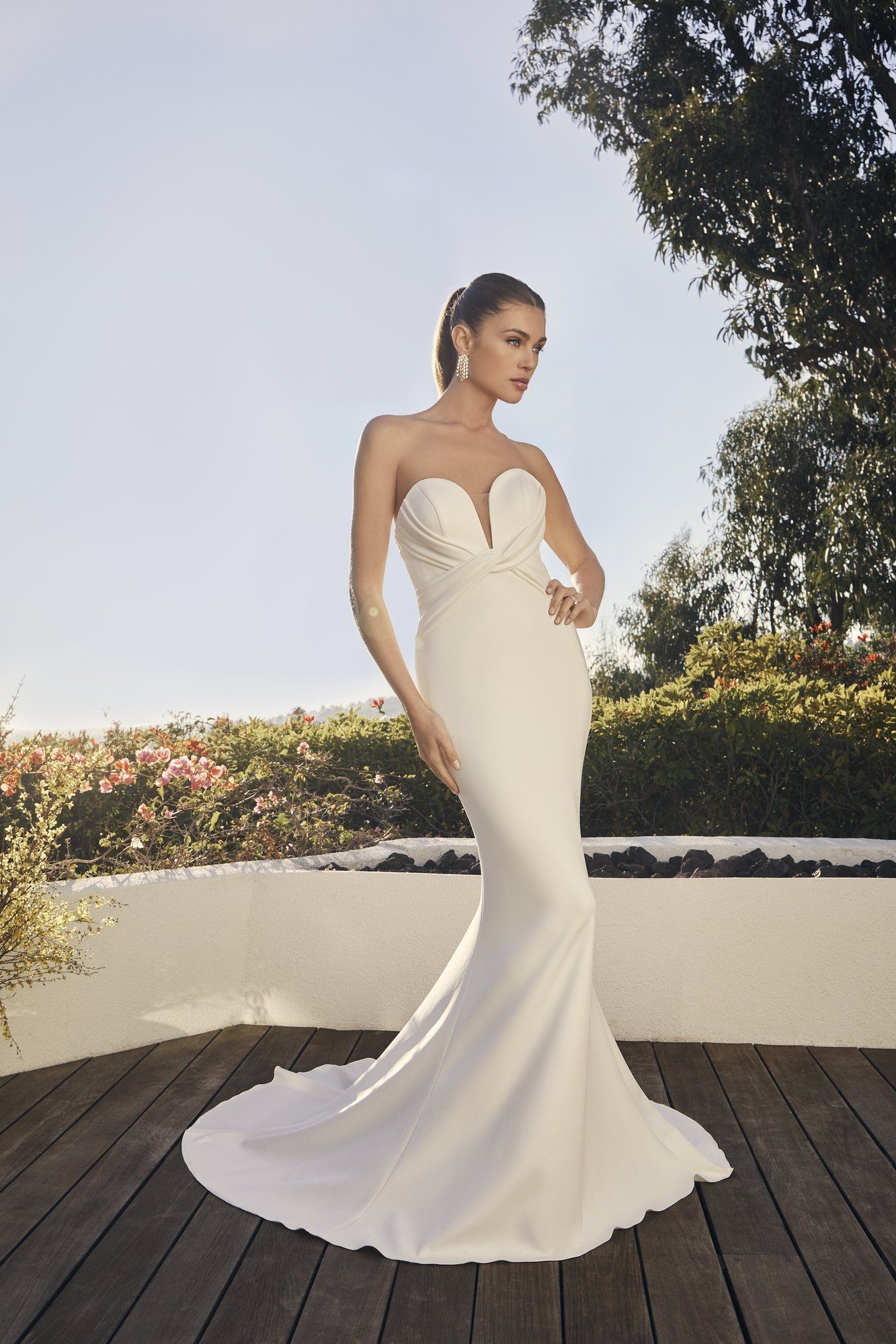 A woman in a white wedding dress is standing on a wooden deck.