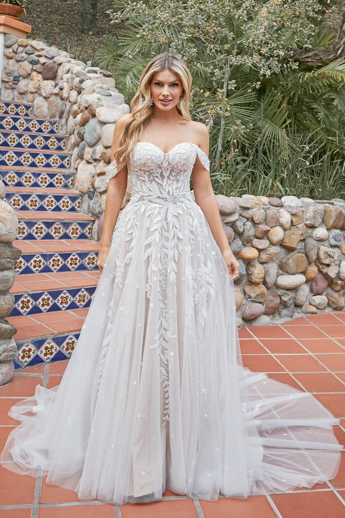 A woman in a white wedding dress is standing in front of a stone wall.
