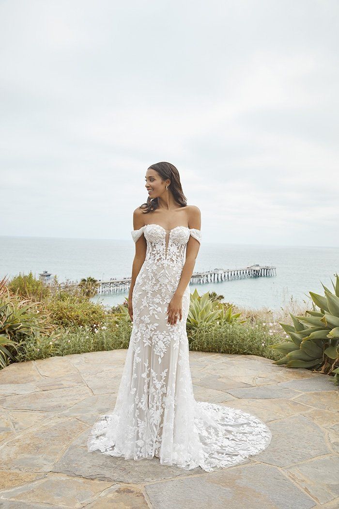 A woman in a white wedding dress is standing in front of the ocean.