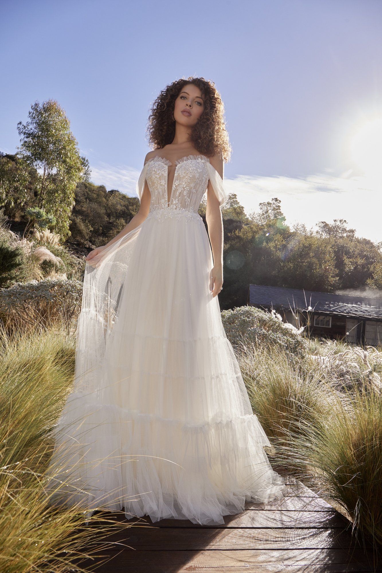 A woman in a white wedding dress is standing on a wooden bridge.