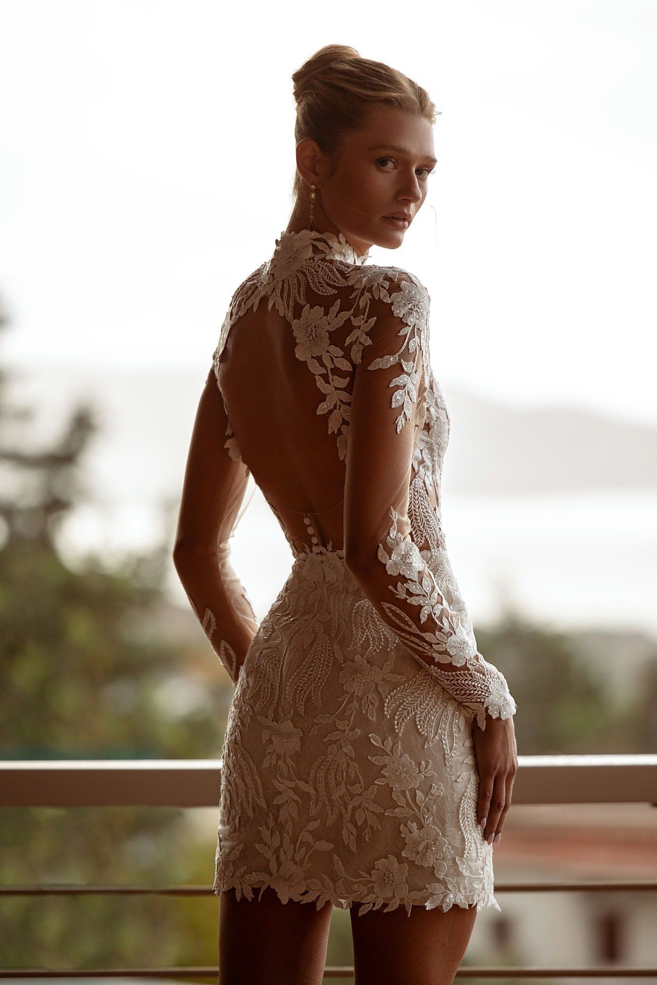 A woman in a short wedding dress is standing on a balcony.