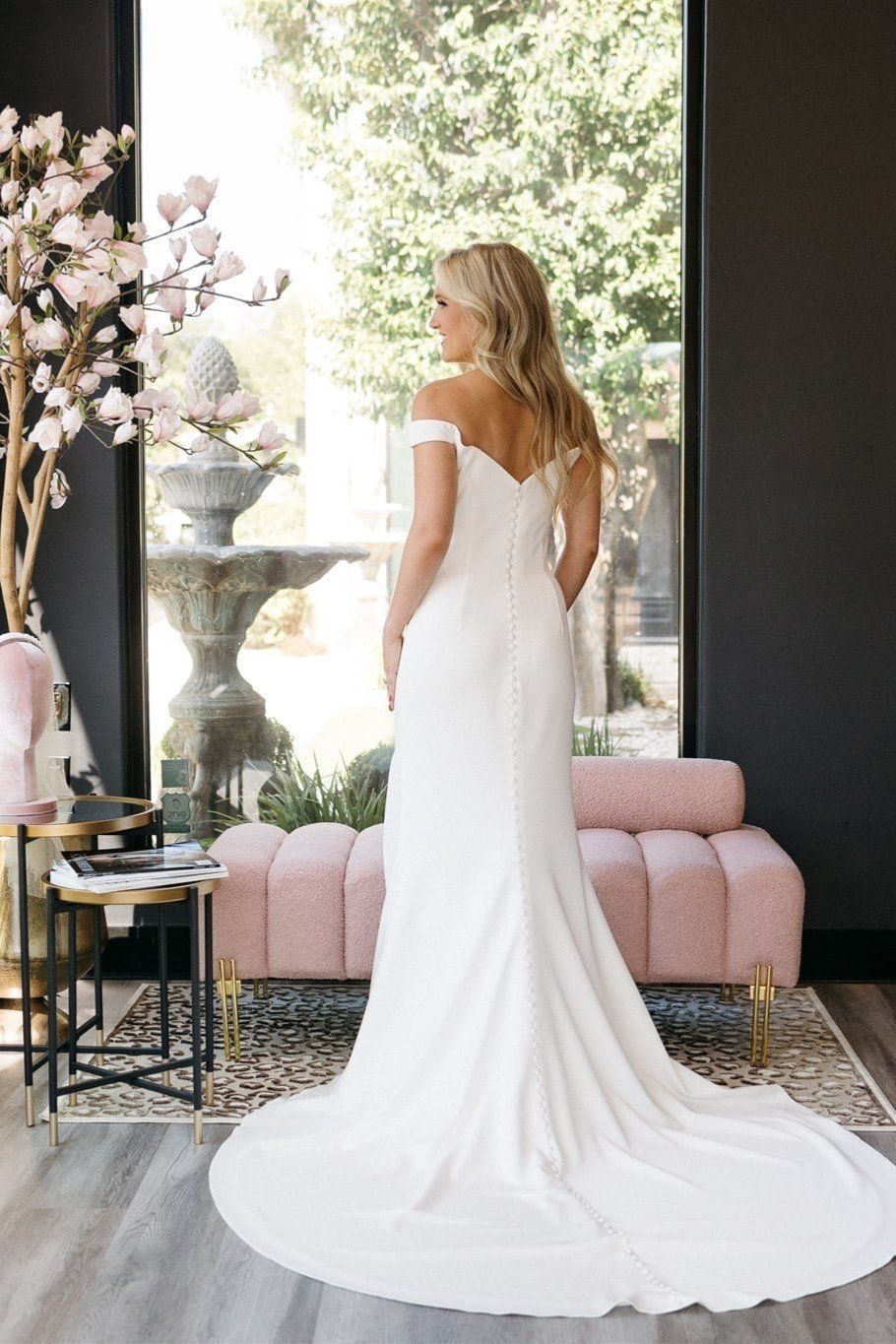A woman in a white wedding dress is standing in front of a window.