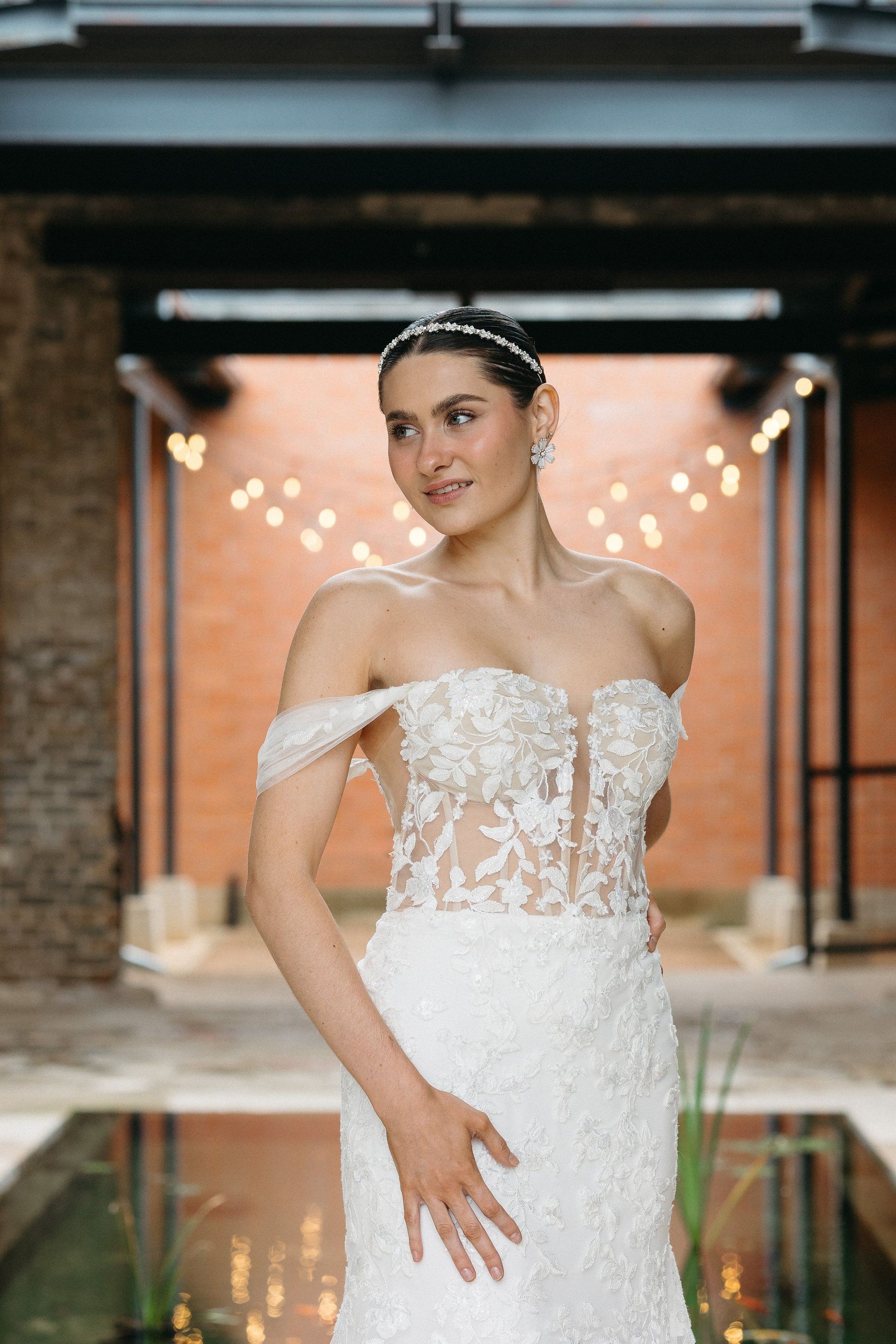 A woman in a white wedding dress is standing in front of a pond.