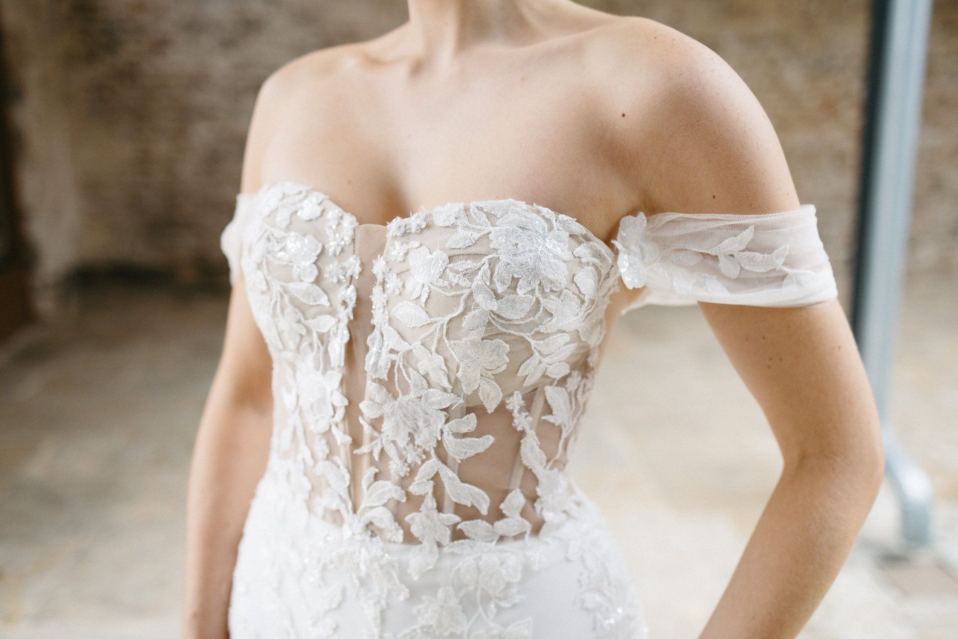 A woman is wearing a white lace wedding dress with off the shoulder sleeves.