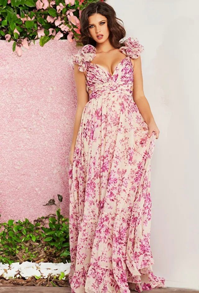 A woman in a long pink floral dress is standing in front of a pink wall.