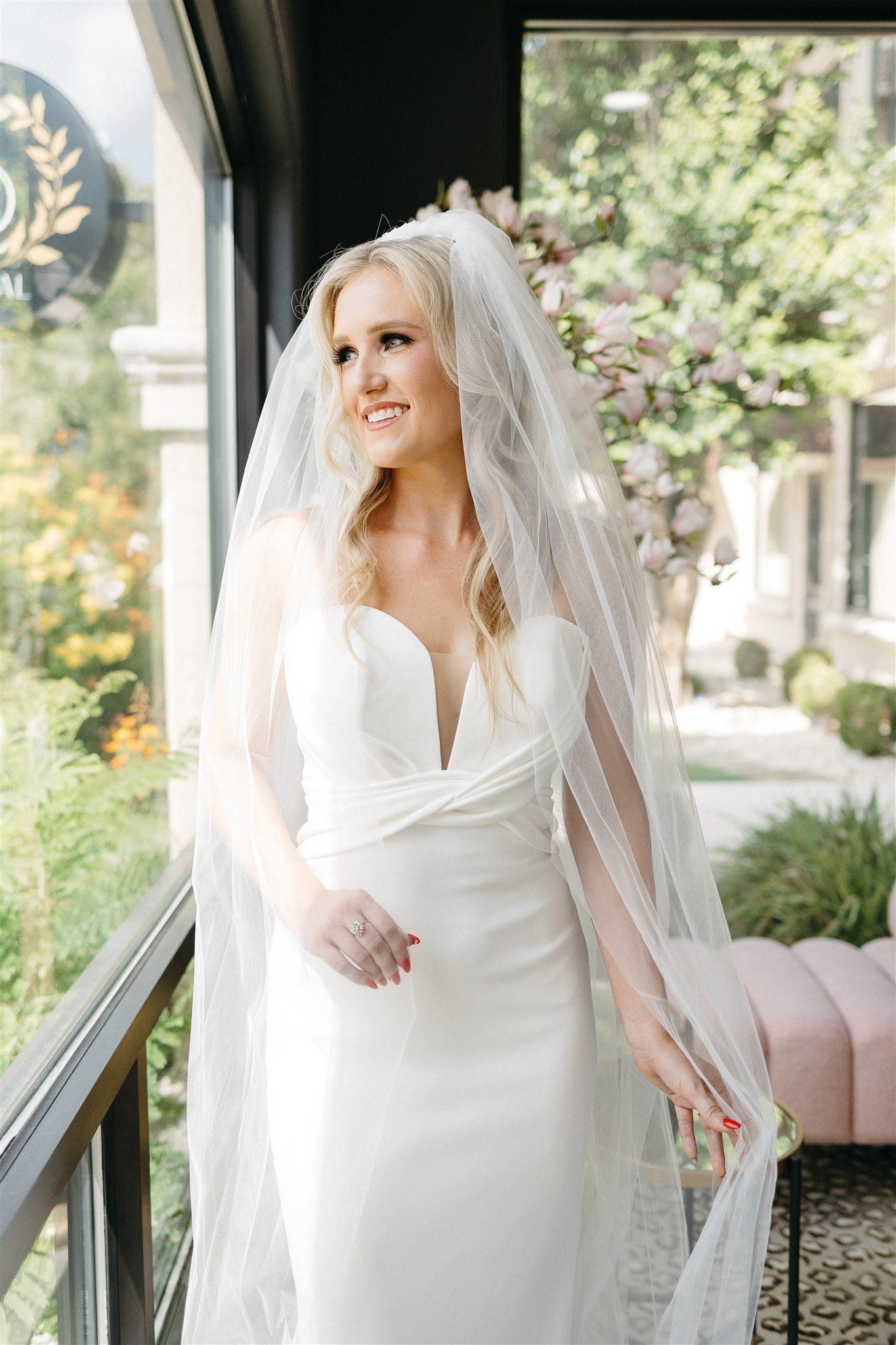 A bride in a white dress and veil is standing in front of a window.