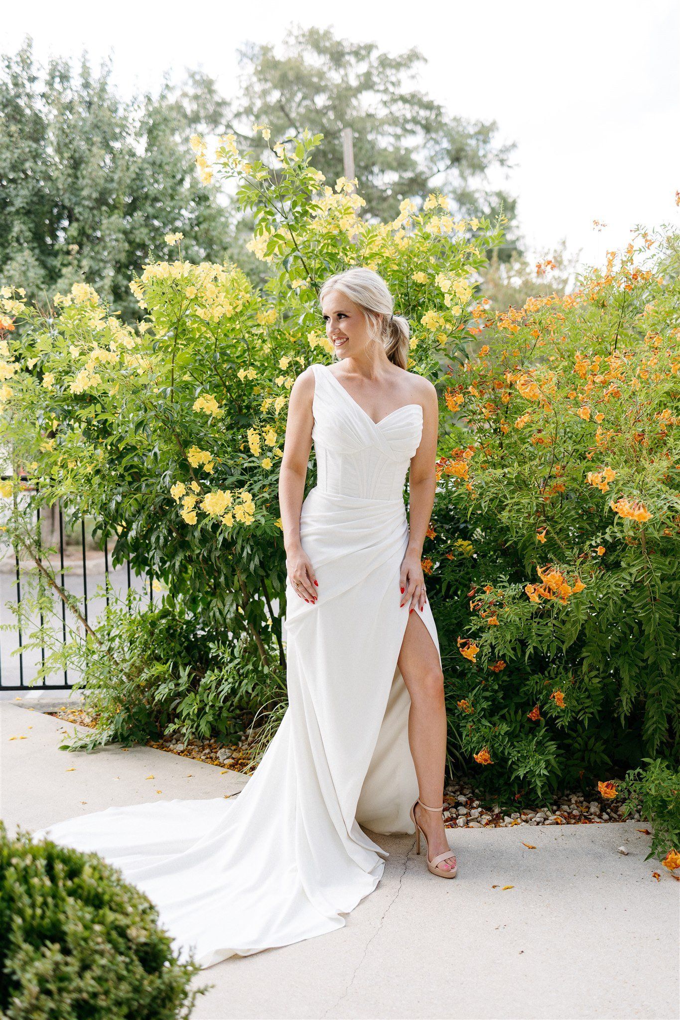 A woman in a white wedding dress is standing in front of a bush.