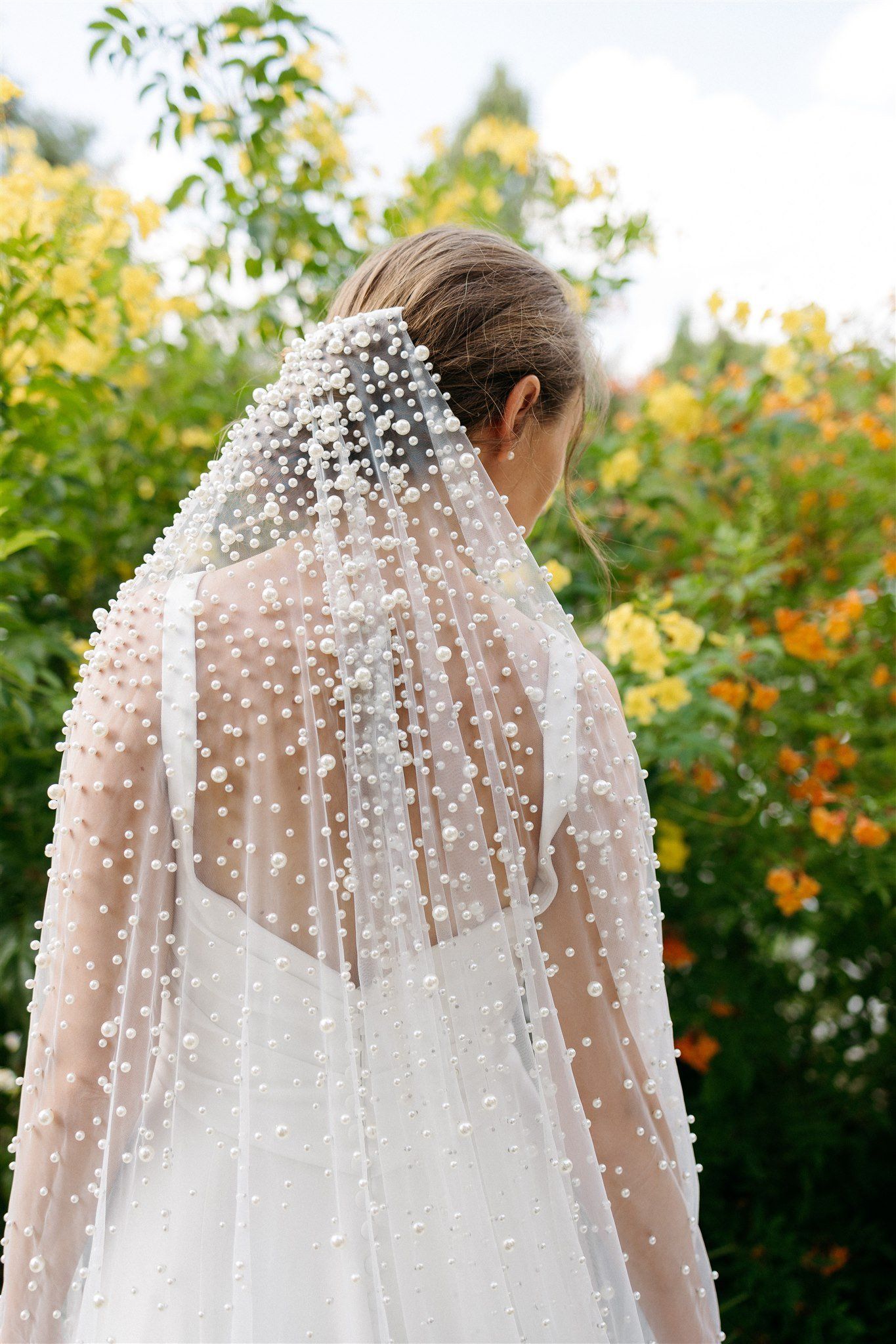 The back of a bride wearing a veil with pearls on it.
