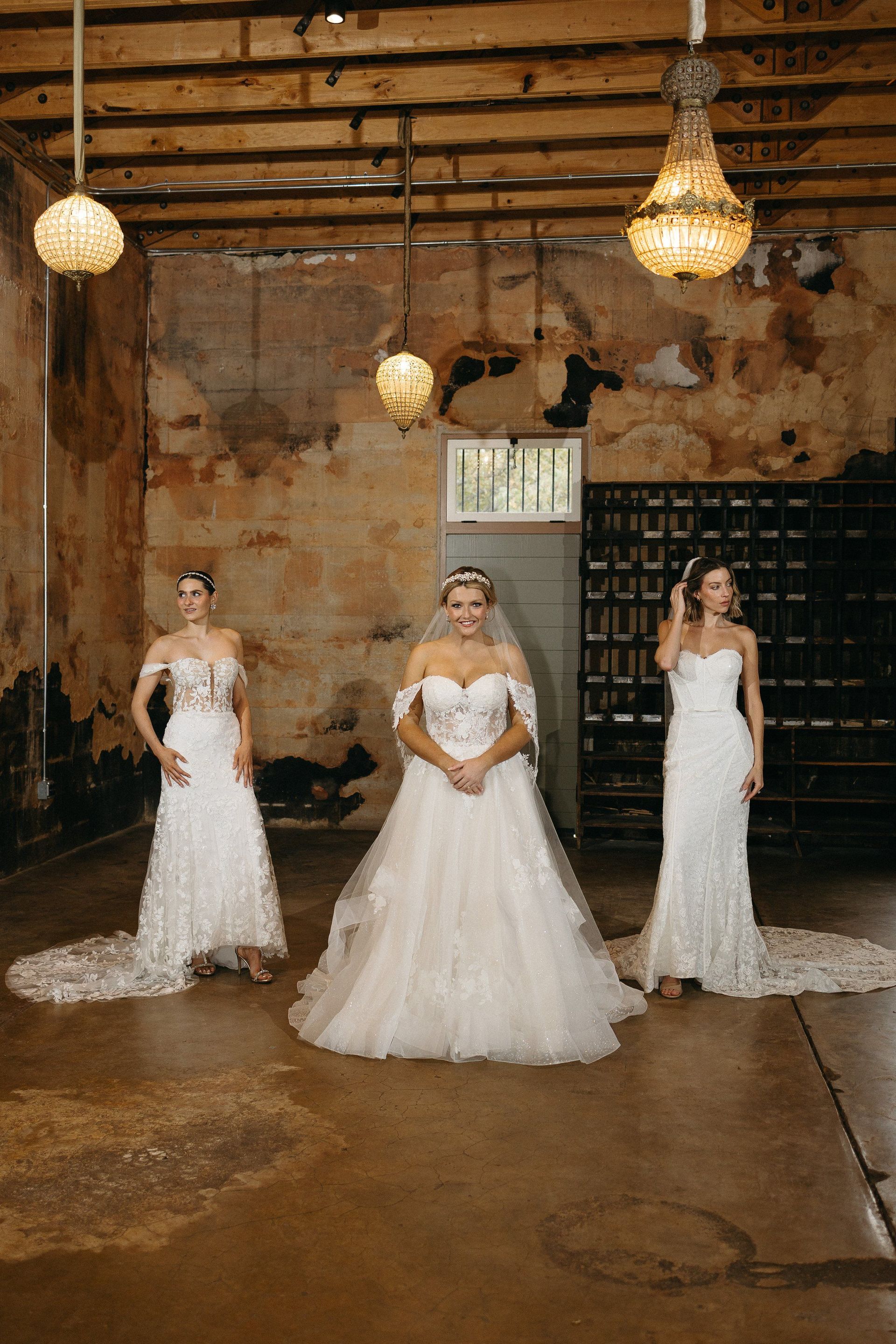 Three women in wedding dresses are standing next to each other in a room.