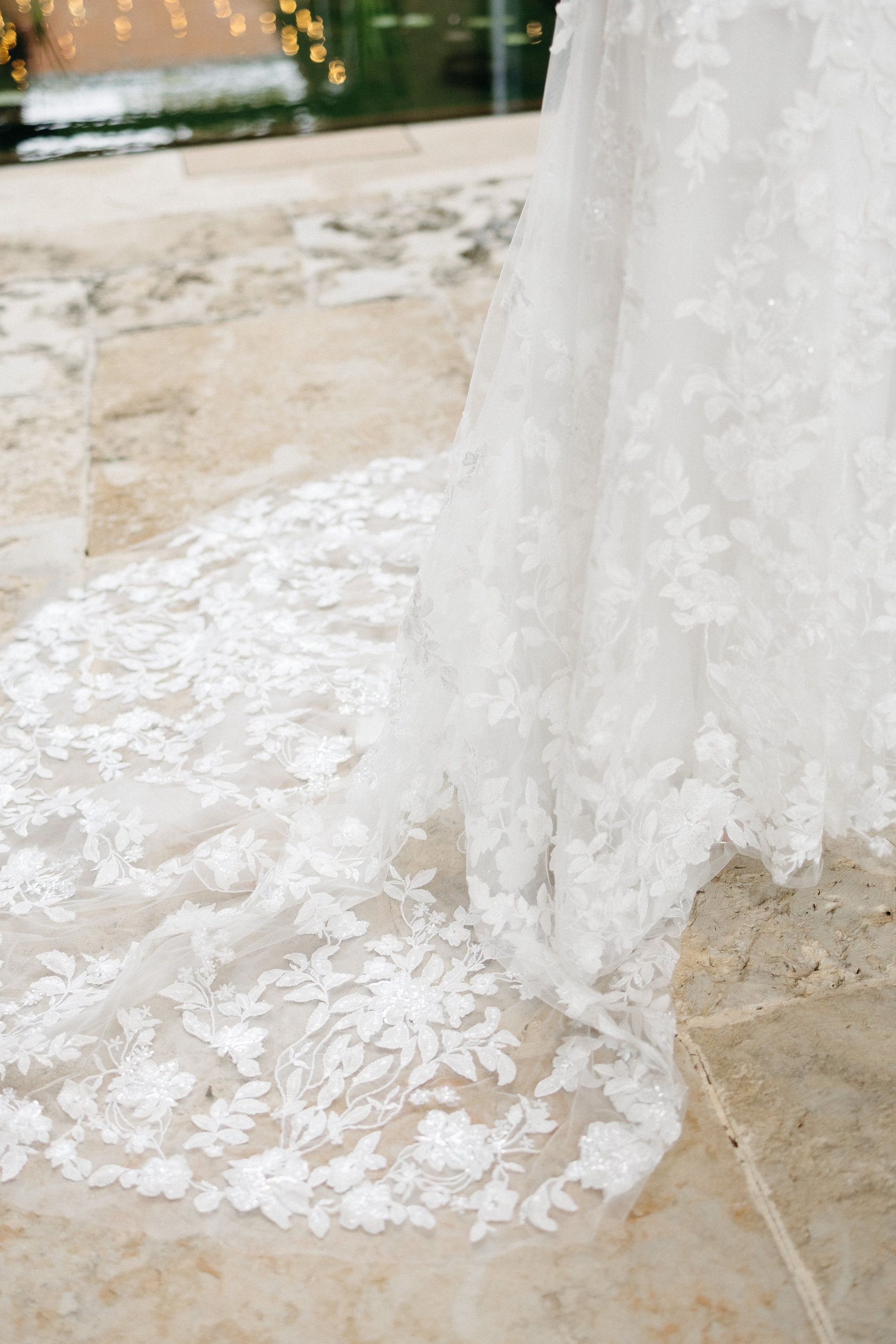 A bride in a white lace wedding dress is standing on a tiled floor.