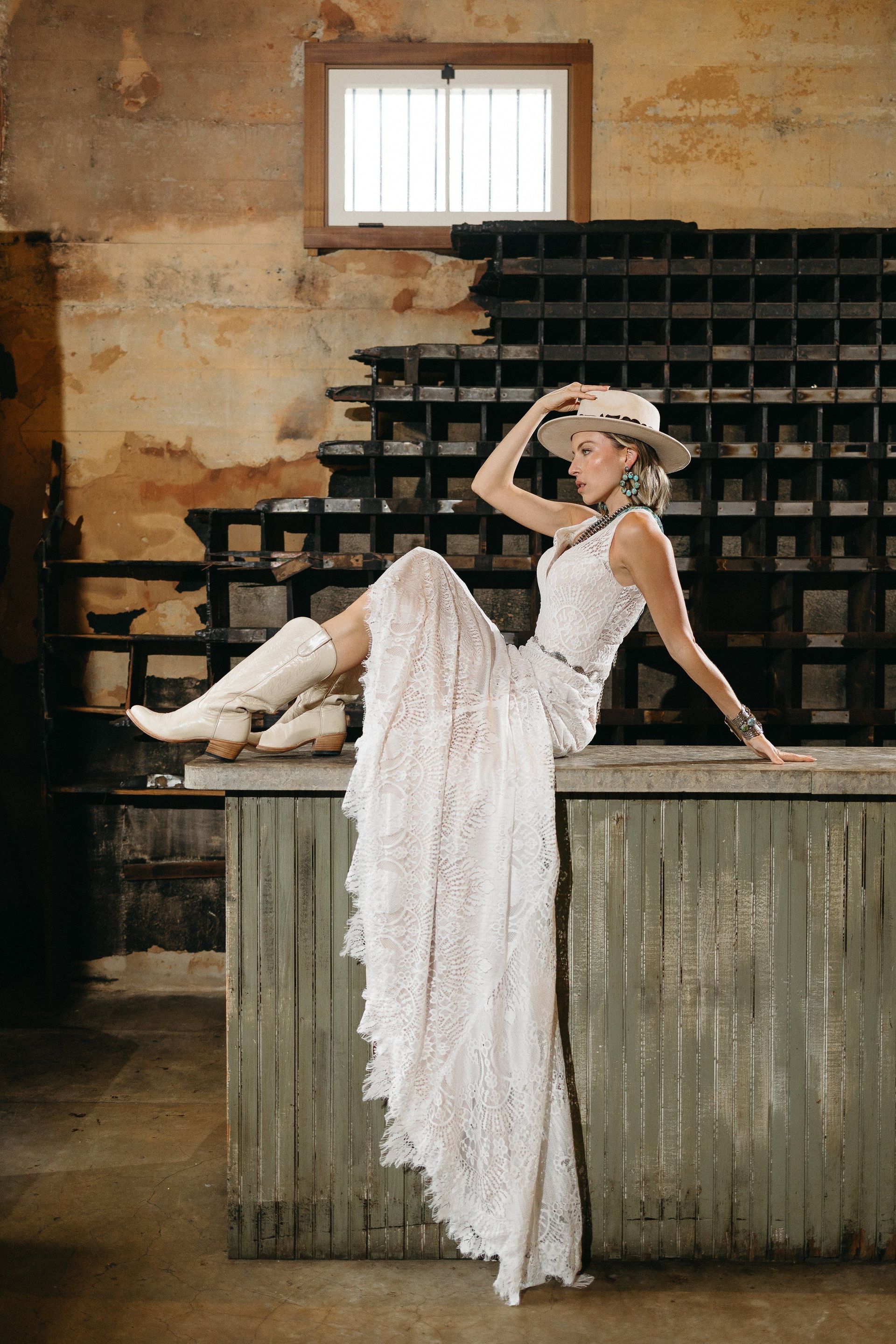 A woman in a wedding dress and cowboy boots is sitting on a counter.