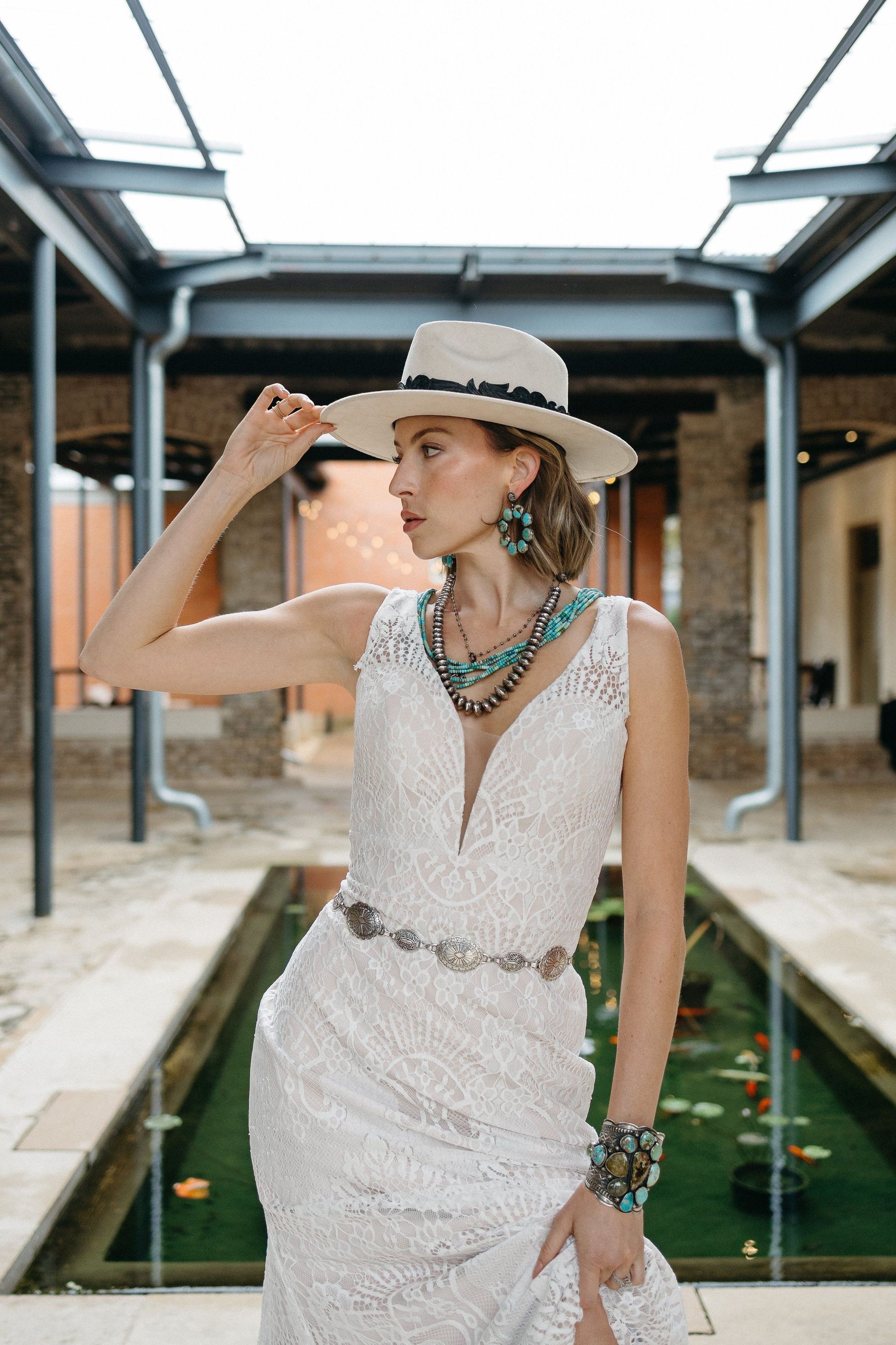 A woman in a white dress and hat is standing in front of a pond.