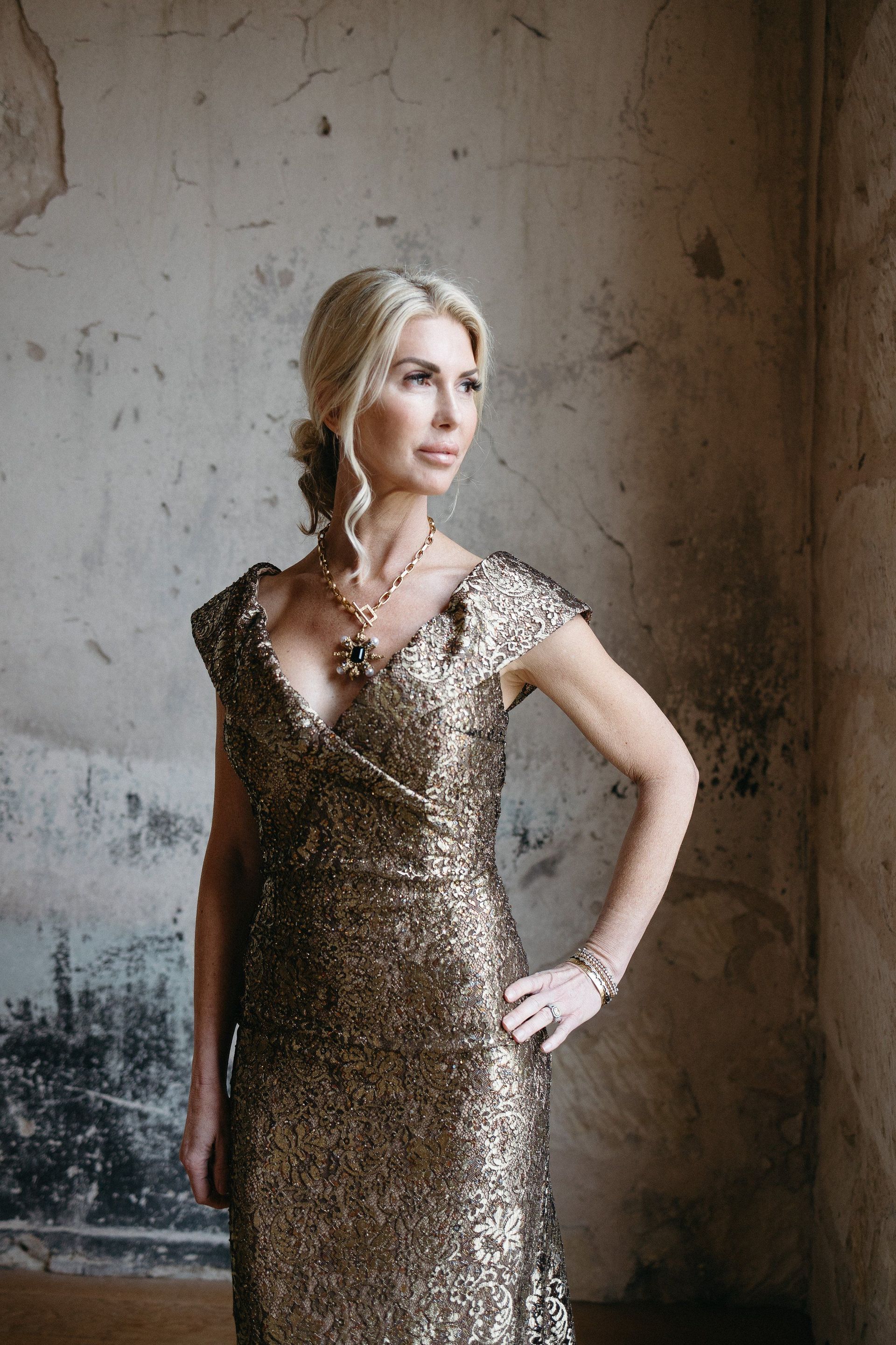 A woman in a gold dress is standing in front of a wall.
