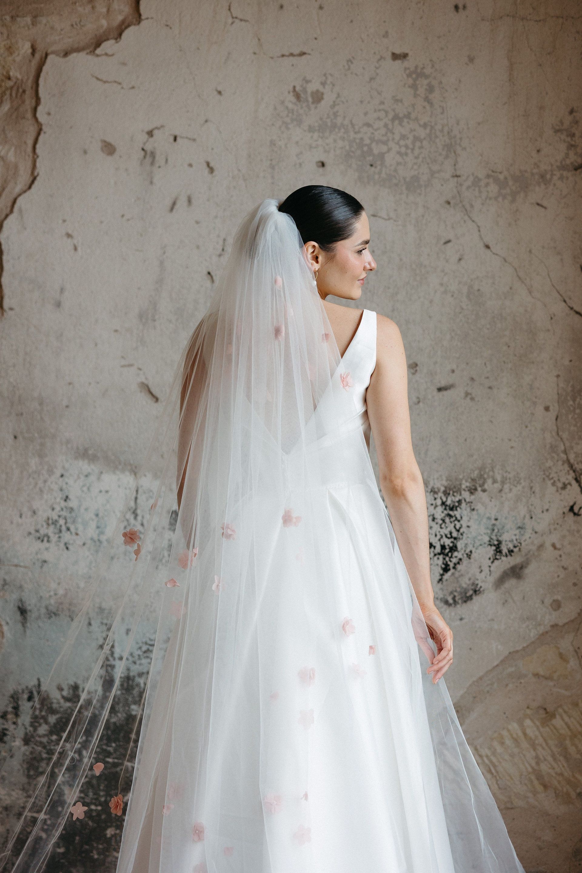 A woman in a wedding dress and veil is standing in front of a wall.