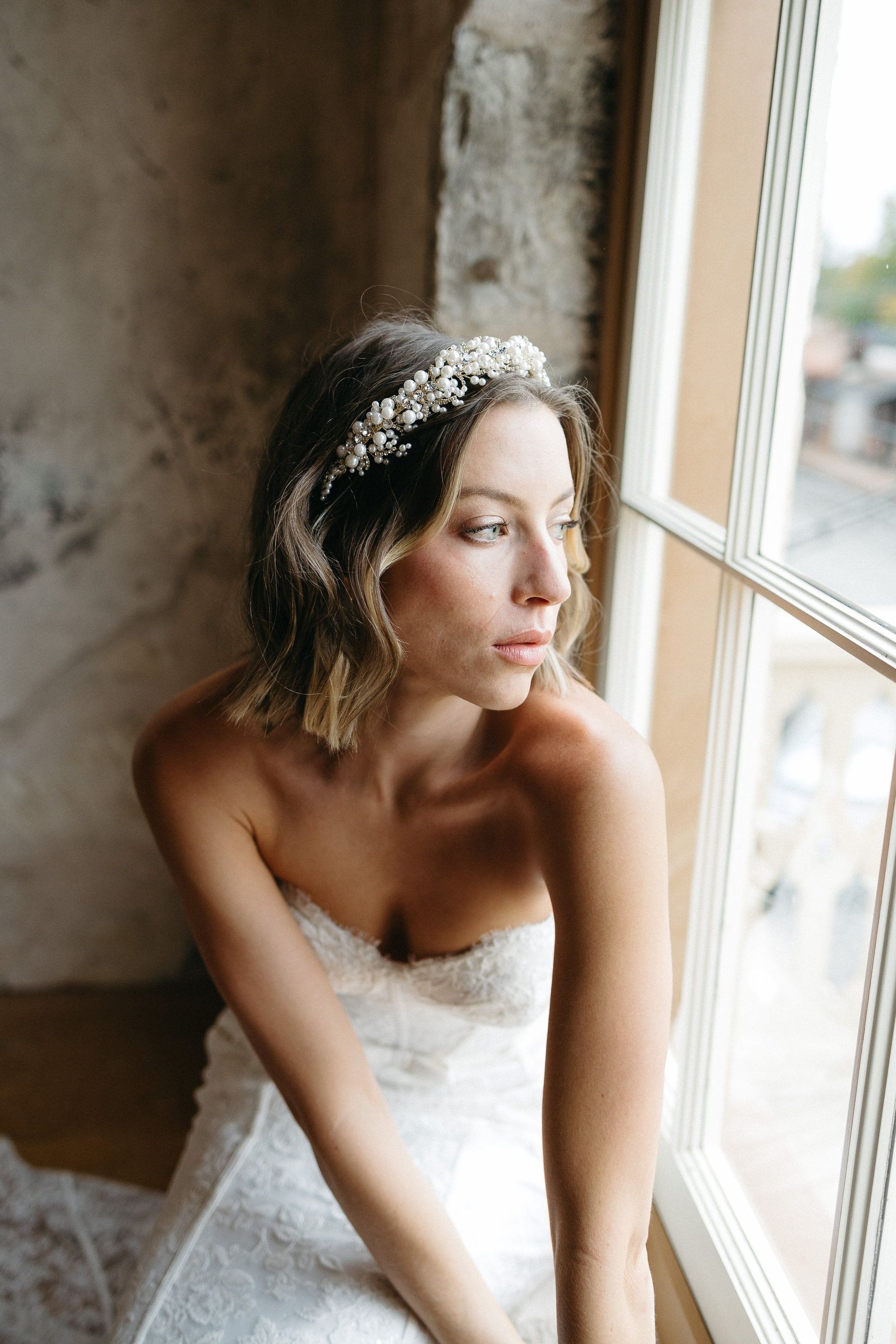 A woman in a wedding dress is sitting in front of a window.