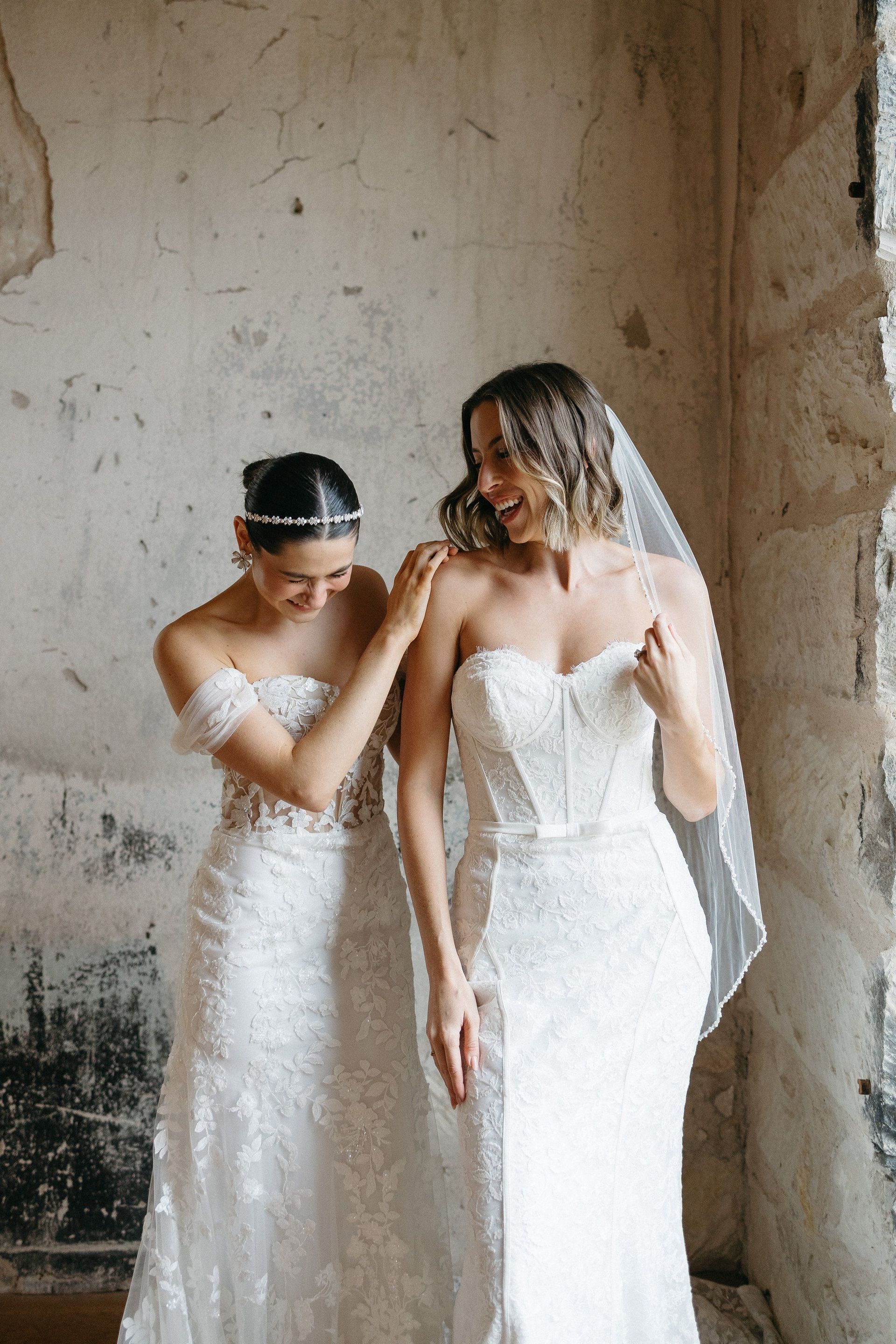 Two women in wedding dresses are standing next to each other in a room.