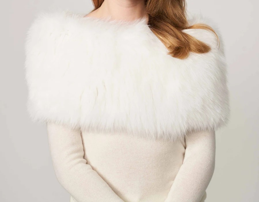A woman wearing a white sweater and a white fur cape.