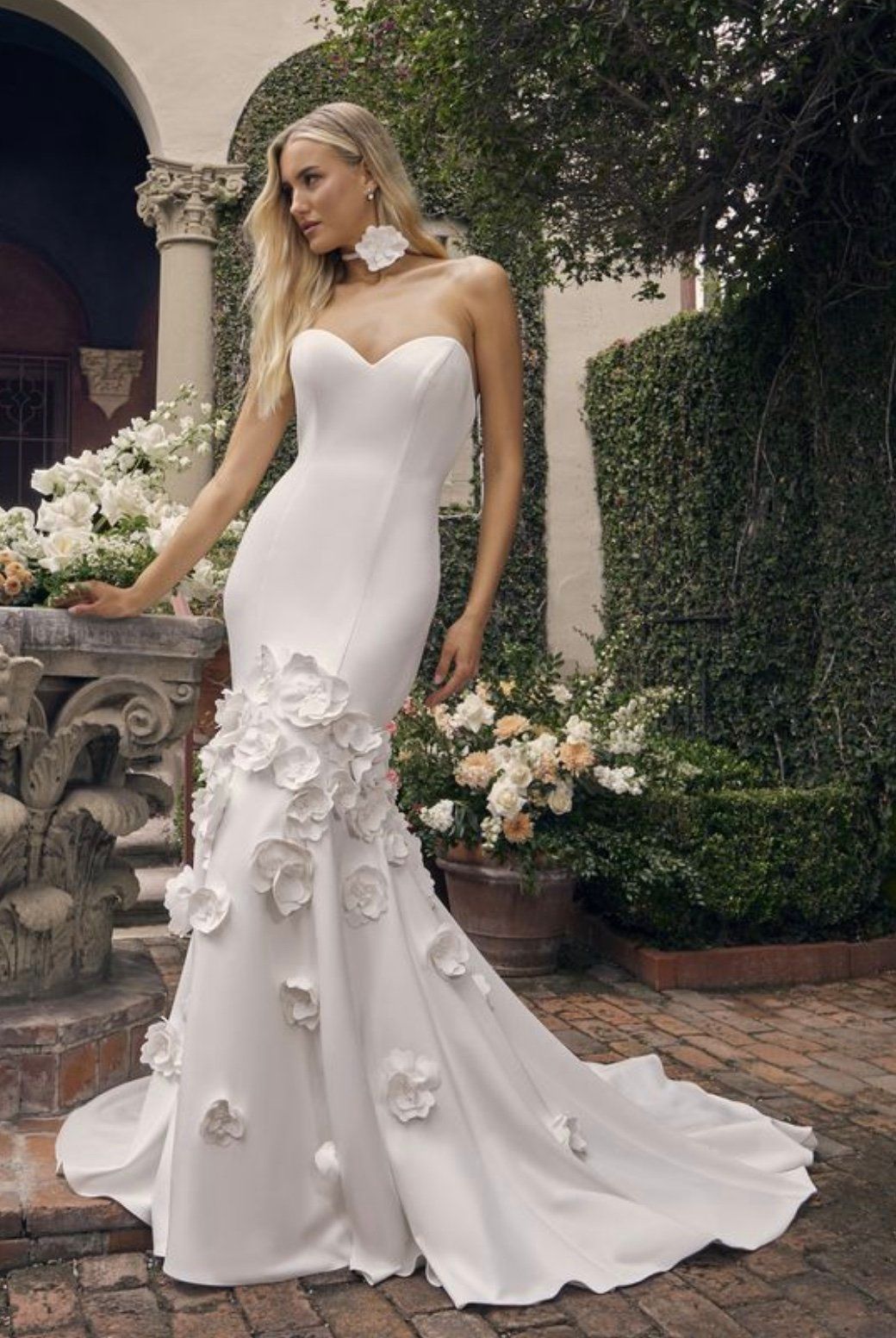 A woman is wearing a white wedding dress with flowers on the skirt.