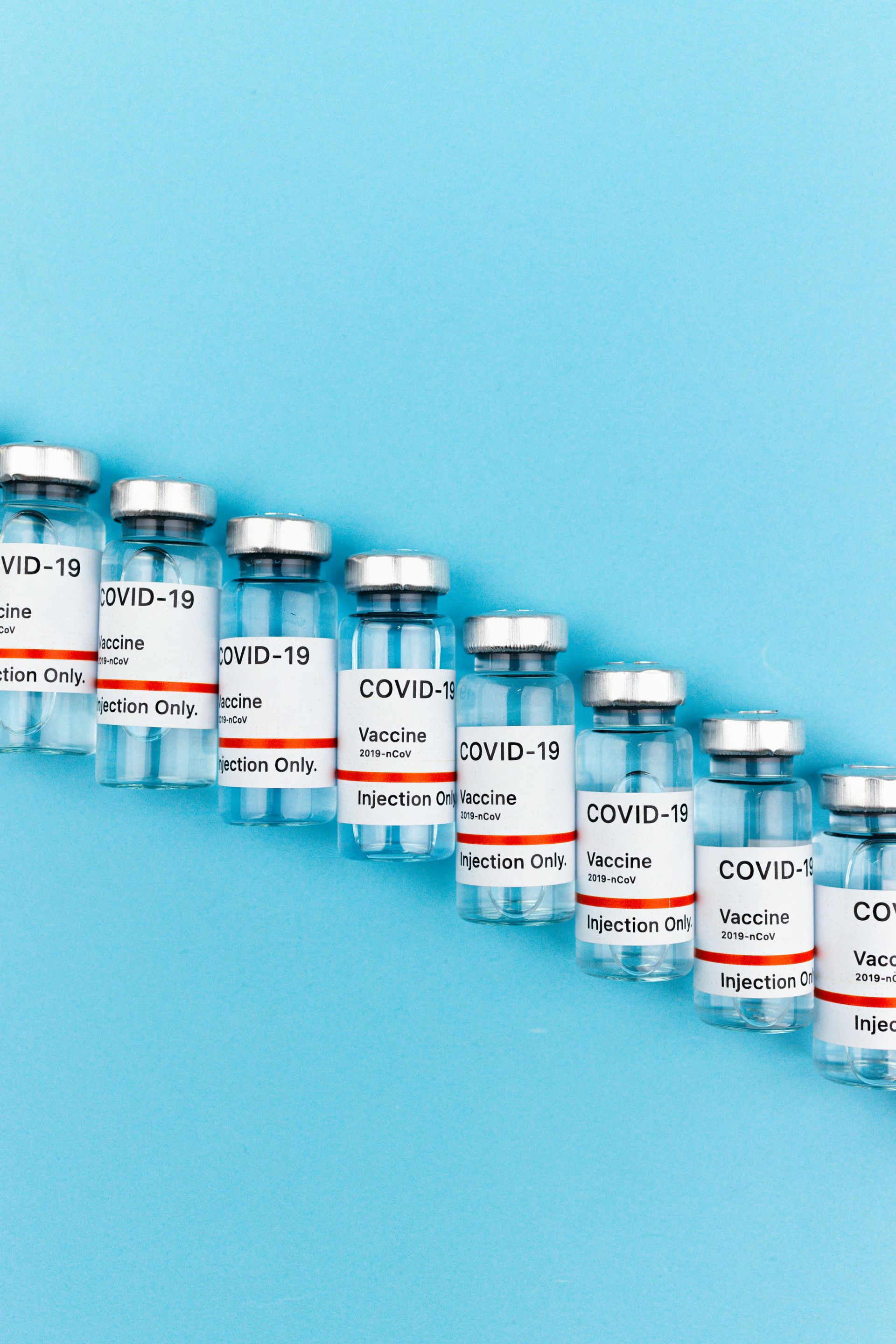 A row of bottles of vaccine are lined up on a blue surface.