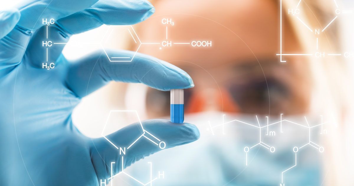 A scientist is holding a blue and white pill in his hand.