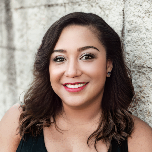 A woman in a black tank top is smiling and standing in front of a wall.