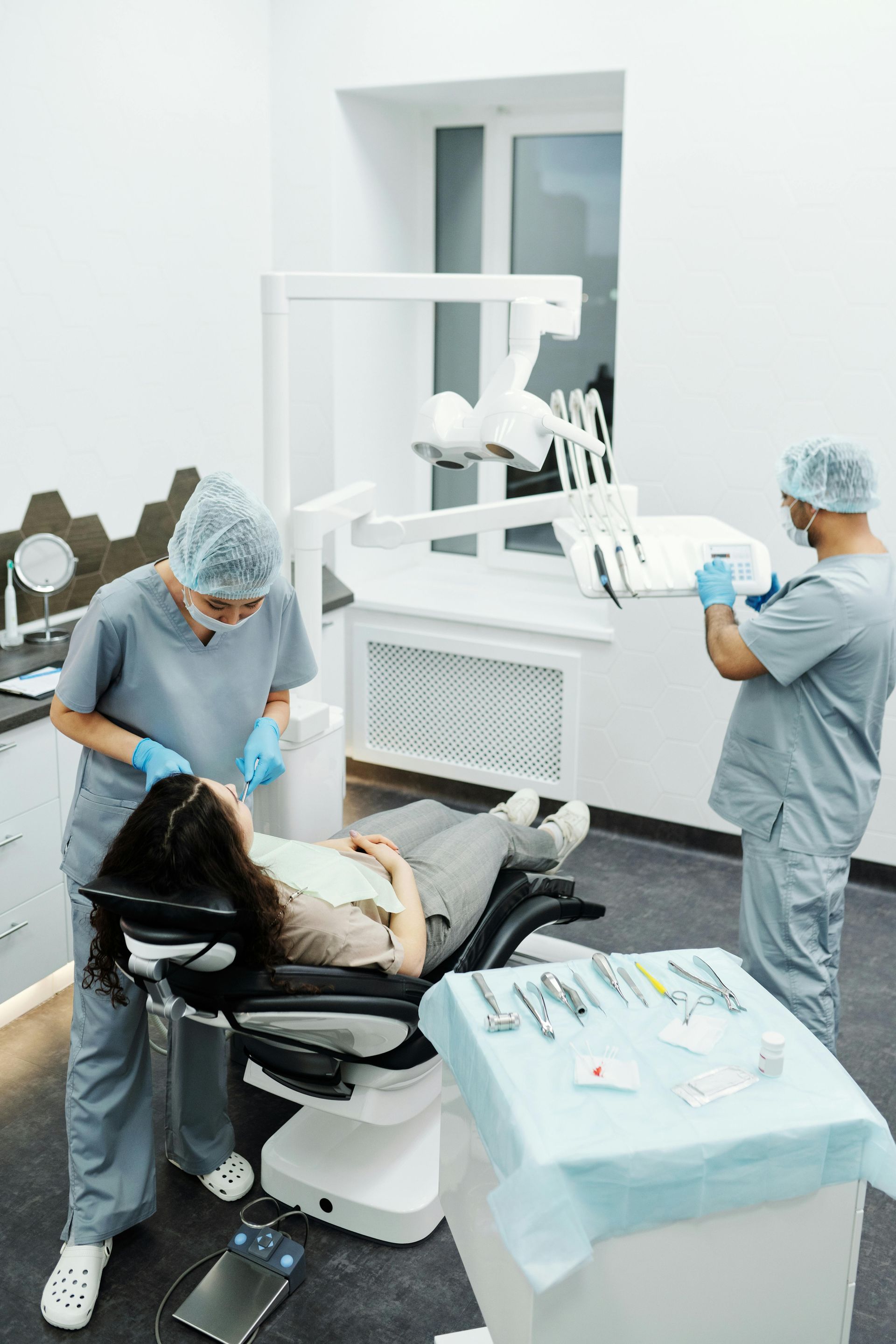 A woman is sitting in a dental chair while two dentists work on her teeth.