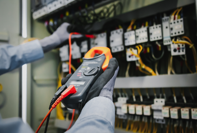 Electrician using a clamp meter to test wires inside an electrical panel.
