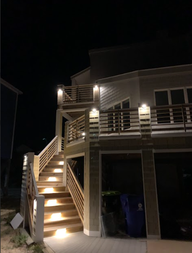 Night view of a two-story house with illuminated stairs and balconies, set against a dark sky.