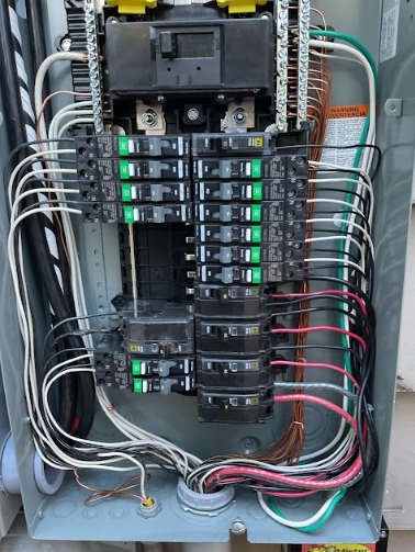 Electrical panel with circuit breakers, wires, and connections inside a metal enclosure.