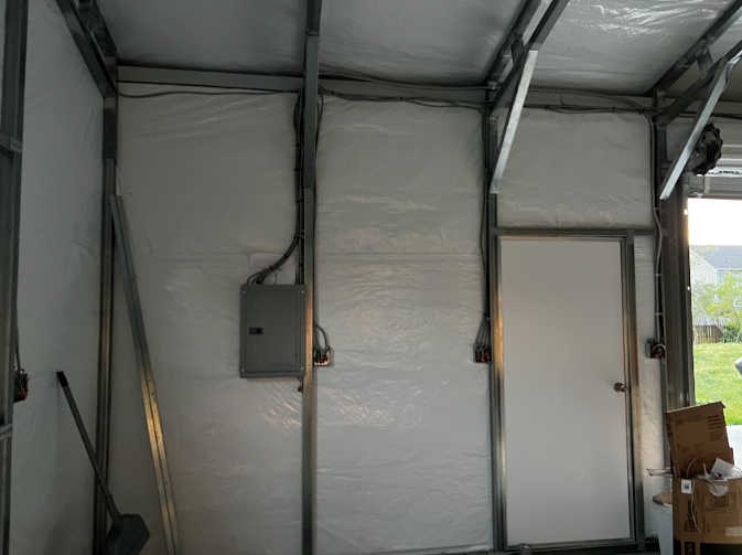 Interior of a metal framed structure with white walls and a door, electrical panel on one wall.