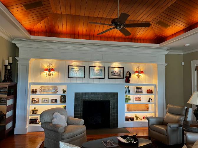 Fireplace with built-in bookshelves, sconces, artwork, and a ceiling fan, illuminated by warm lighting.
