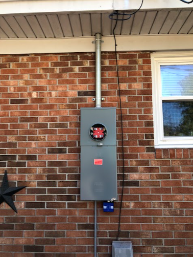 Electrical meter box on a brick wall with conduit running to the roof.