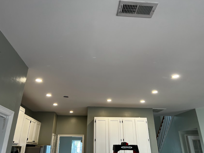 Interior view of a kitchen with white cabinets, green walls, and recessed ceiling lights.