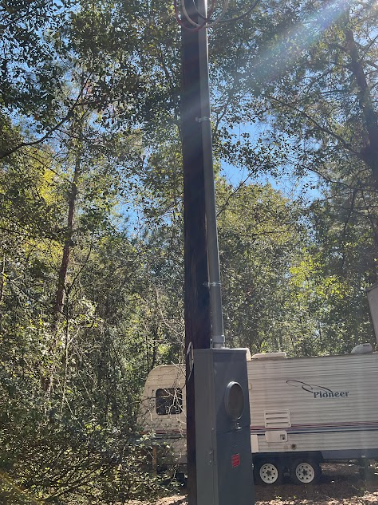 Tall utility pole near a recreational vehicle in a wooded area with blue sky.