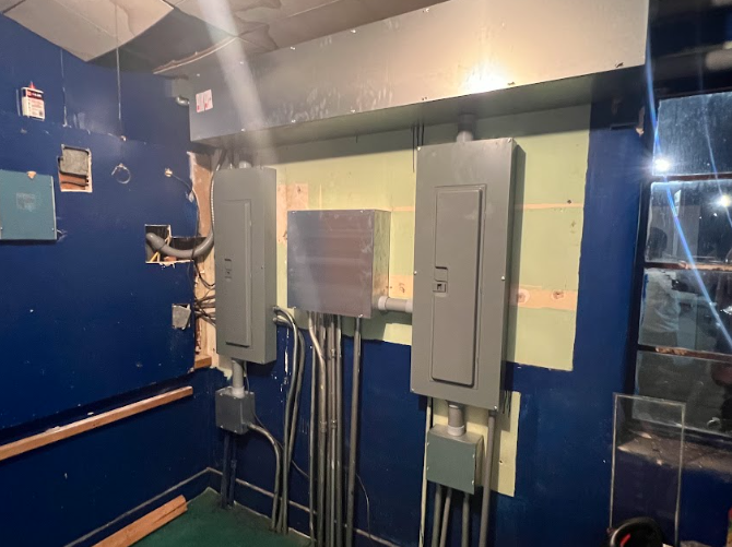 Electrical panels and conduit mounted on a wall in a room with blue paint.