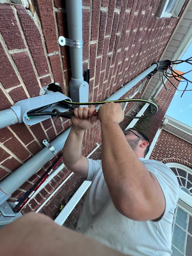 Person using a tool on electrical conduit attached to a brick building.
