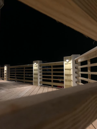 Wooden deck at night with lit posts and horizontal railings.