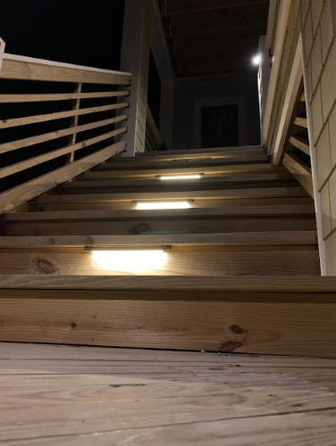 Wooden stairs with integrated lighting leading up to a house entrance at night.