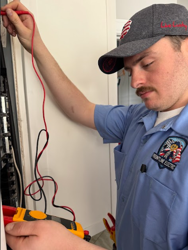 Electrician using a multimeter on an electrical panel. He wears a gray cap and blue uniform.