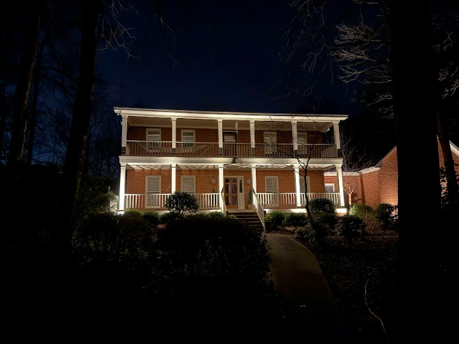 Two-story brick house illuminated at night with a covered porch and walkway, surrounded by dark trees.