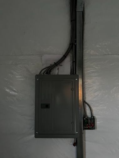 Electrical panel on a white wall with conduit and an adjacent smaller panel.
