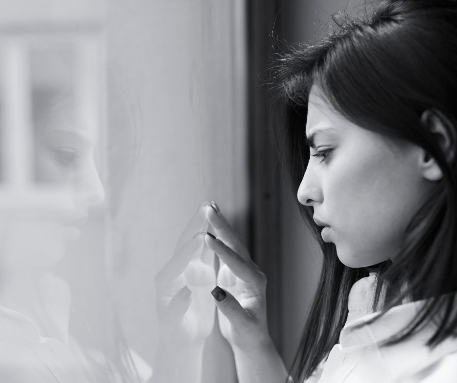 Bereaved woman staring at her reflection in a window