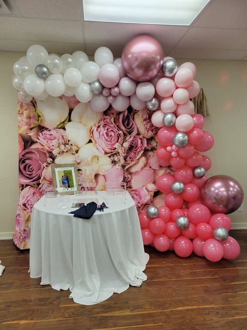 A table is sitting in front of a wall covered in pink and white balloons.