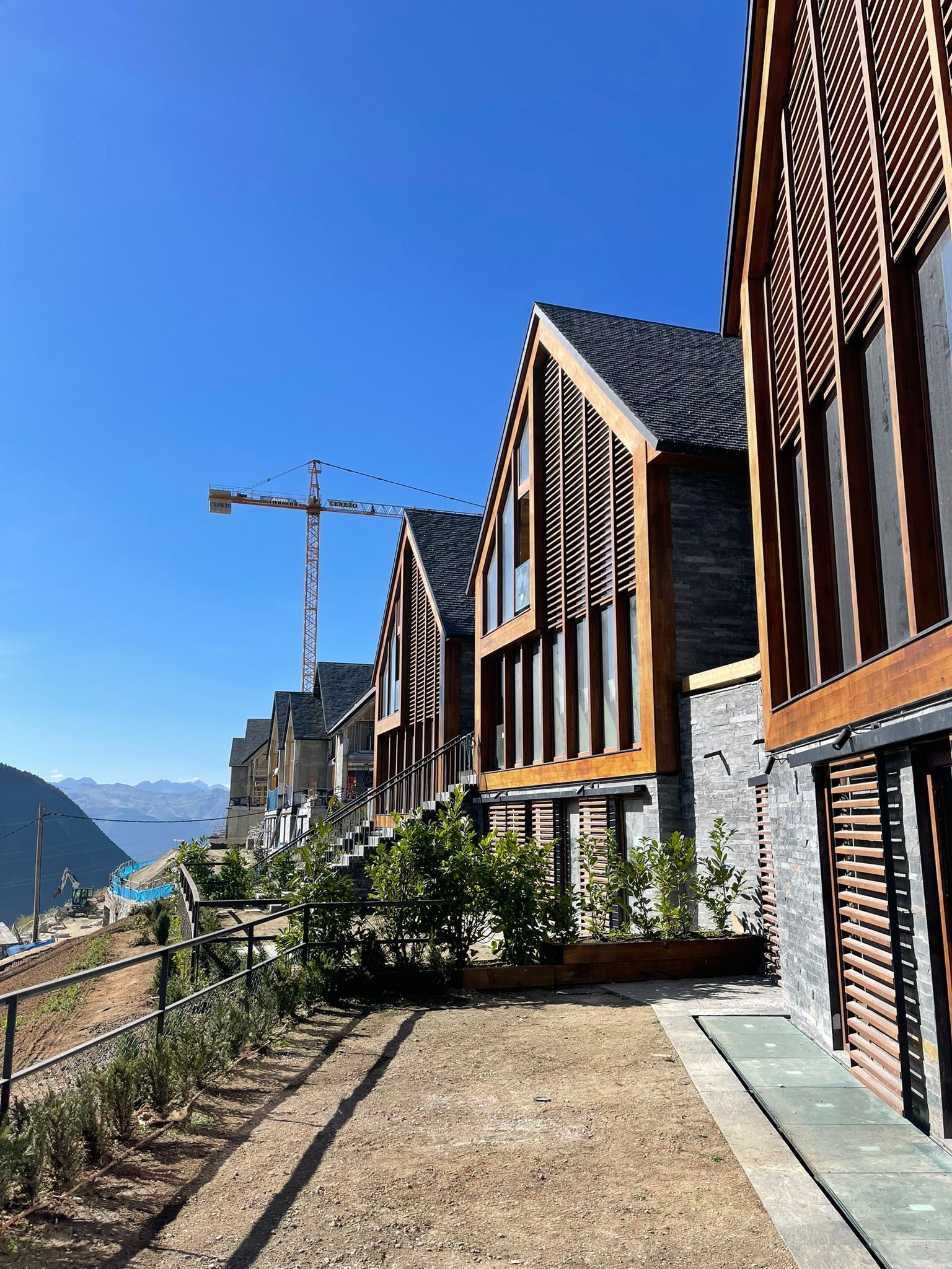 Hilera de casas adosadas modernas con techos inclinados, detalles de madera y paredes de piedra, bajo un cielo azul brillante.