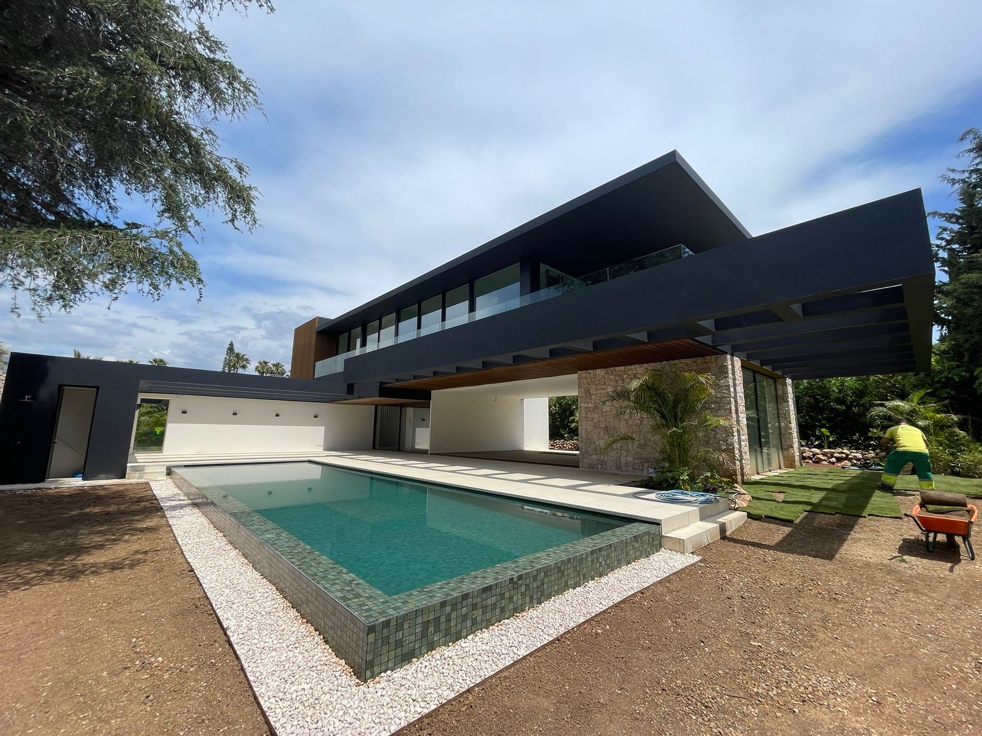 Casa moderna con piscina; exterior oscuro, ventanas grandes, detalles en piedra y un cielo azul claro.