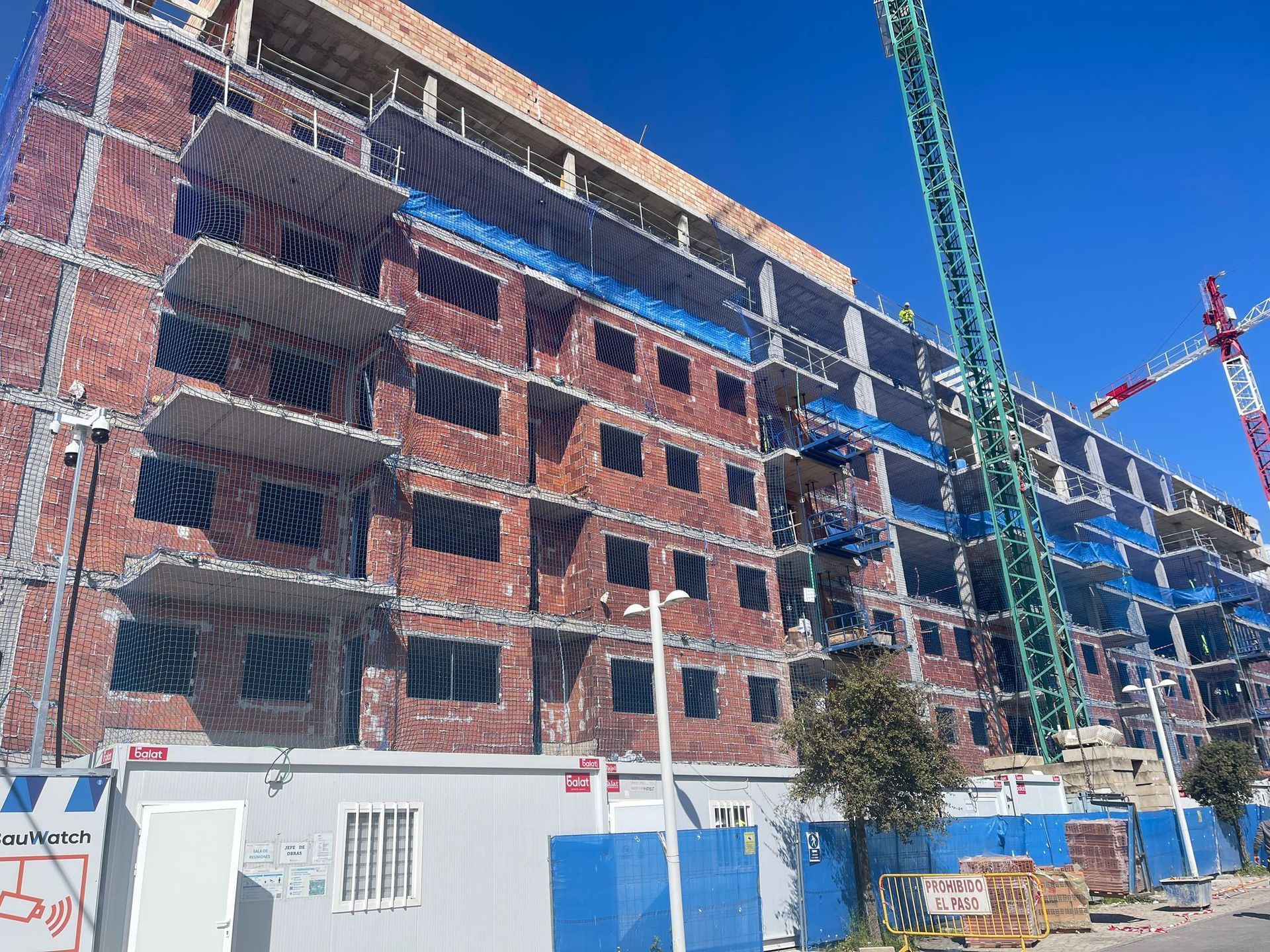 Edificio en construcción con fachada de ladrillo, grúas, redes de seguridad.