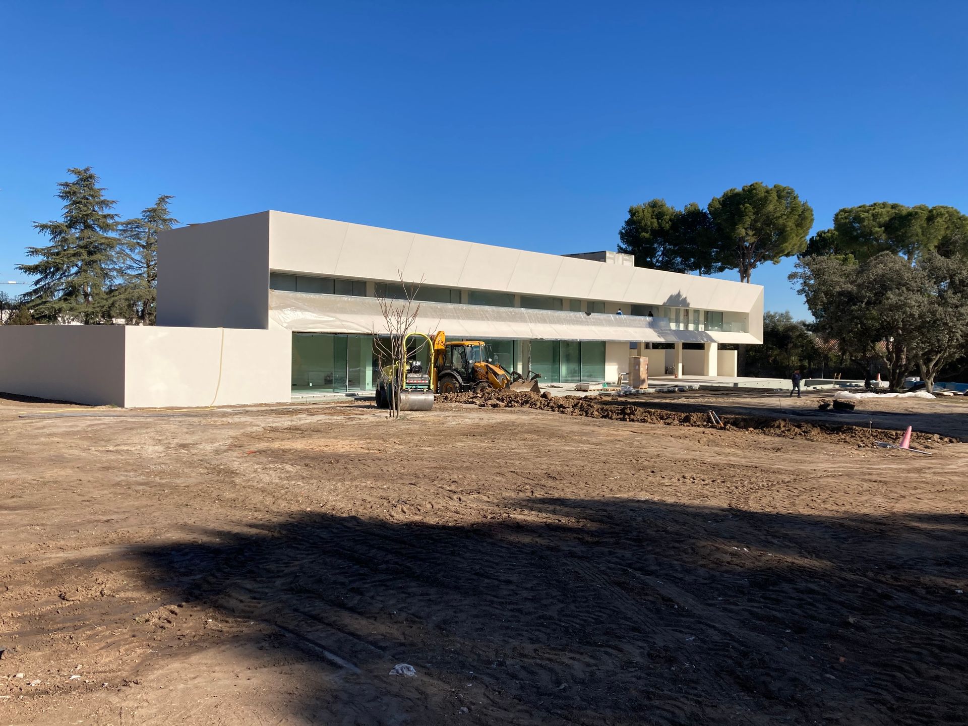 Un edificio moderno de color claro en construcción. Una excavadora trabaja en la tierra frente al edificio en un día soleado.