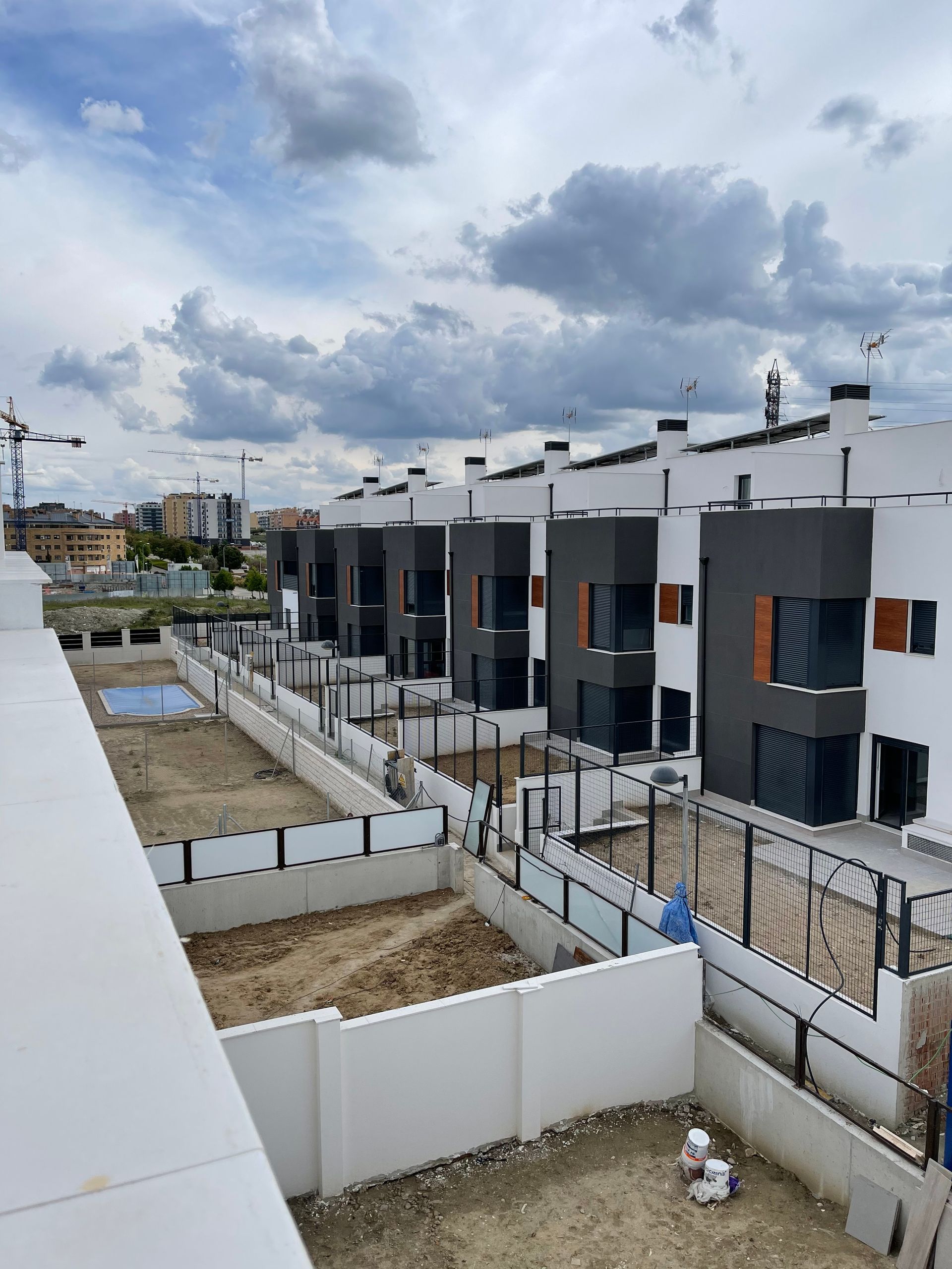 Hilera de casas adosadas modernas con paredes blancas, detalles en gris y pequeños patios cercados bajo un cielo nublado.